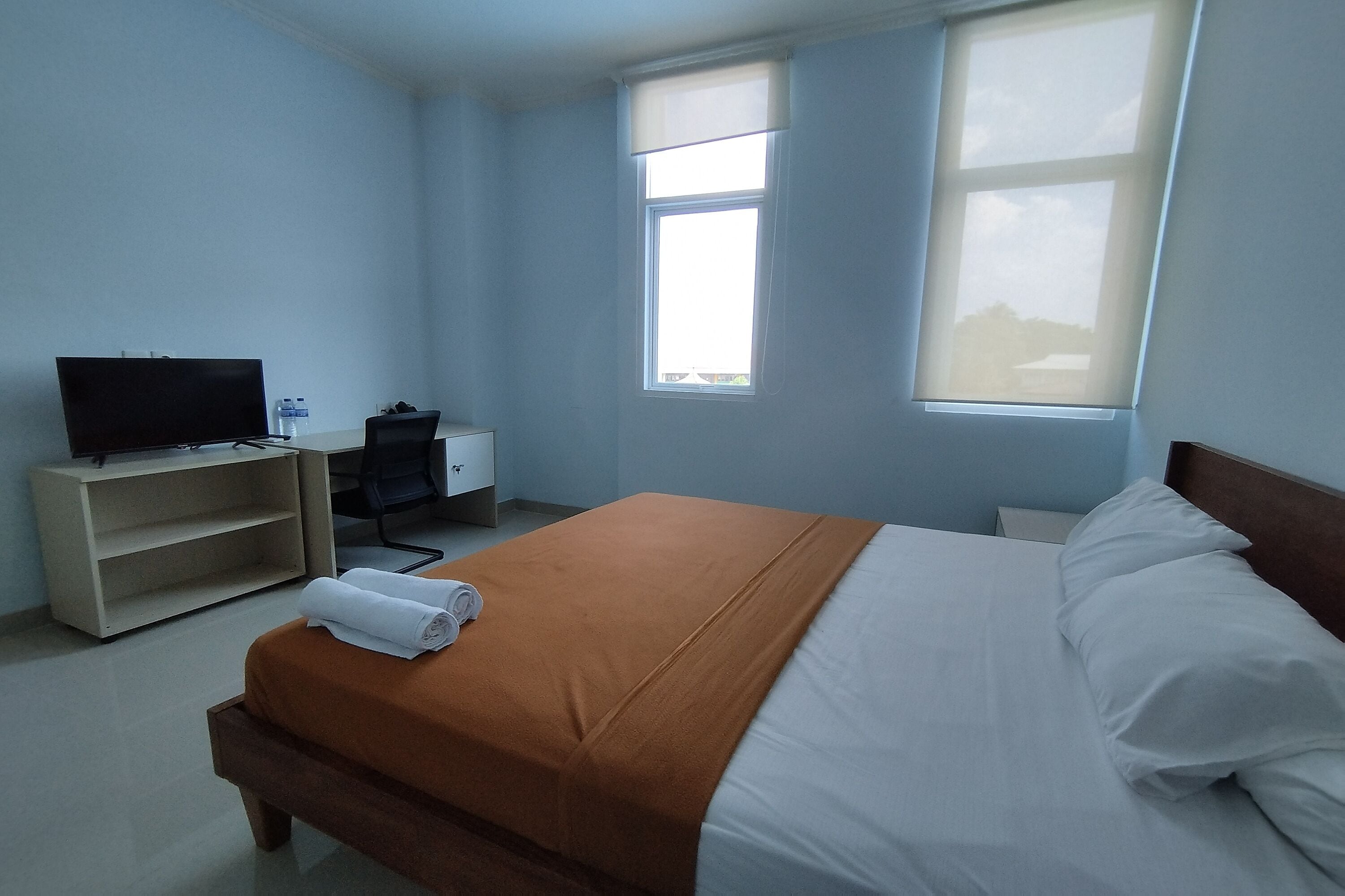 A hotel room with a bed, a desk, a chair, a television, and a window.