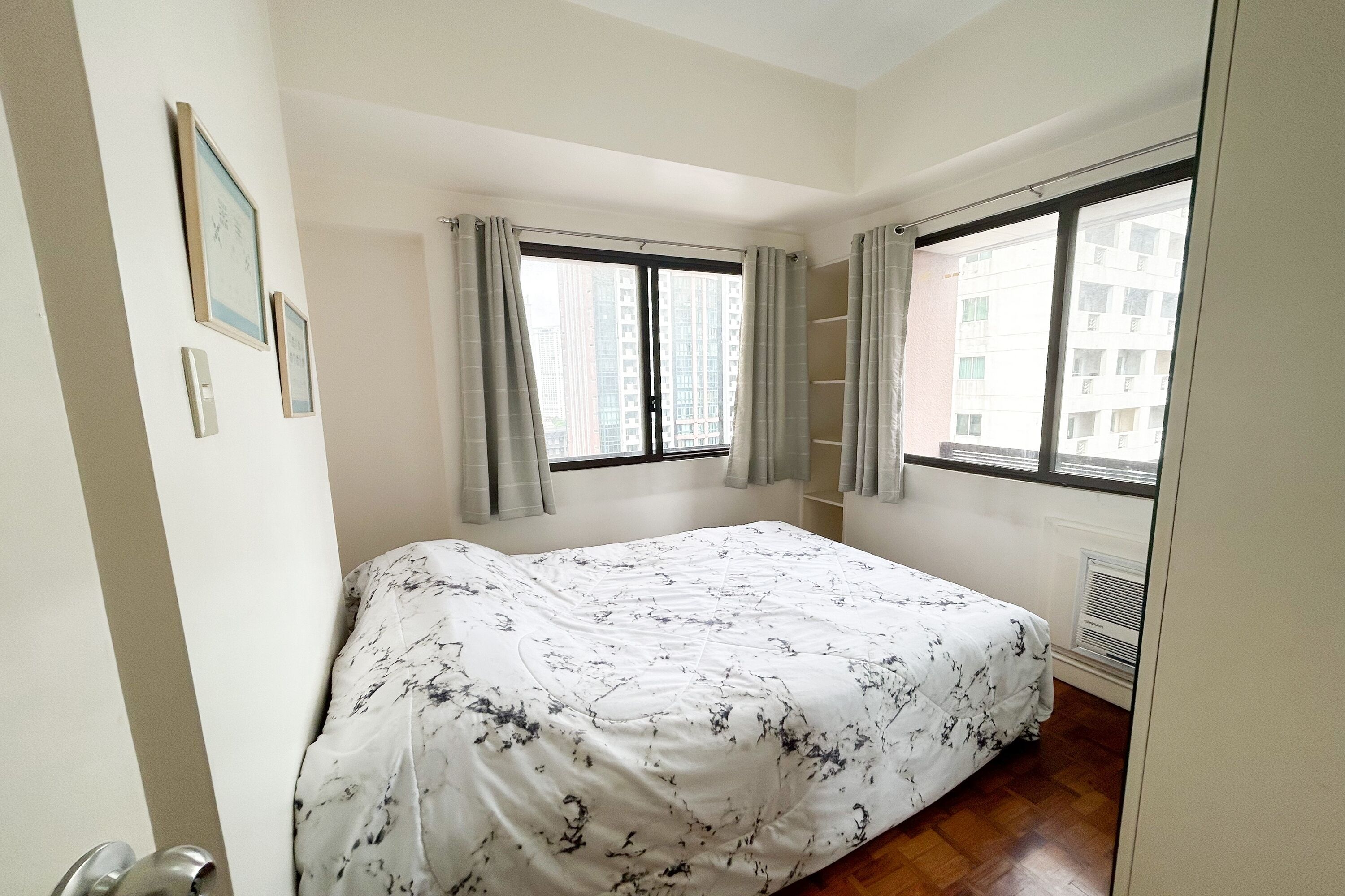 A bedroom with a bed, two windows with curtains, a radiator, and a door.