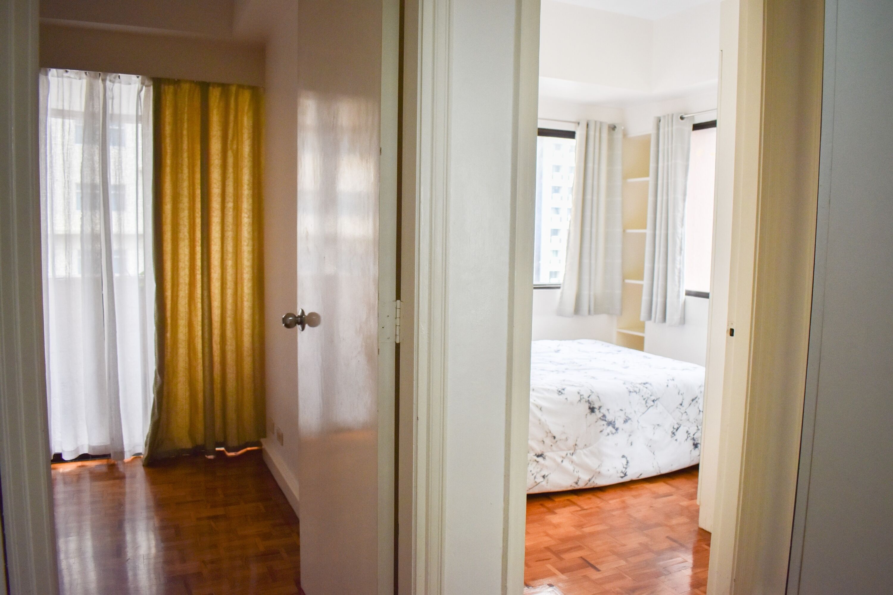 Ein Zimmer mit einem Bett, Holzboden und einer Tür zu einem weiteren Zimmer.