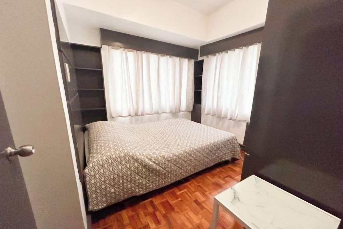 A bedroom with a bed, a desk, and a window with curtains.