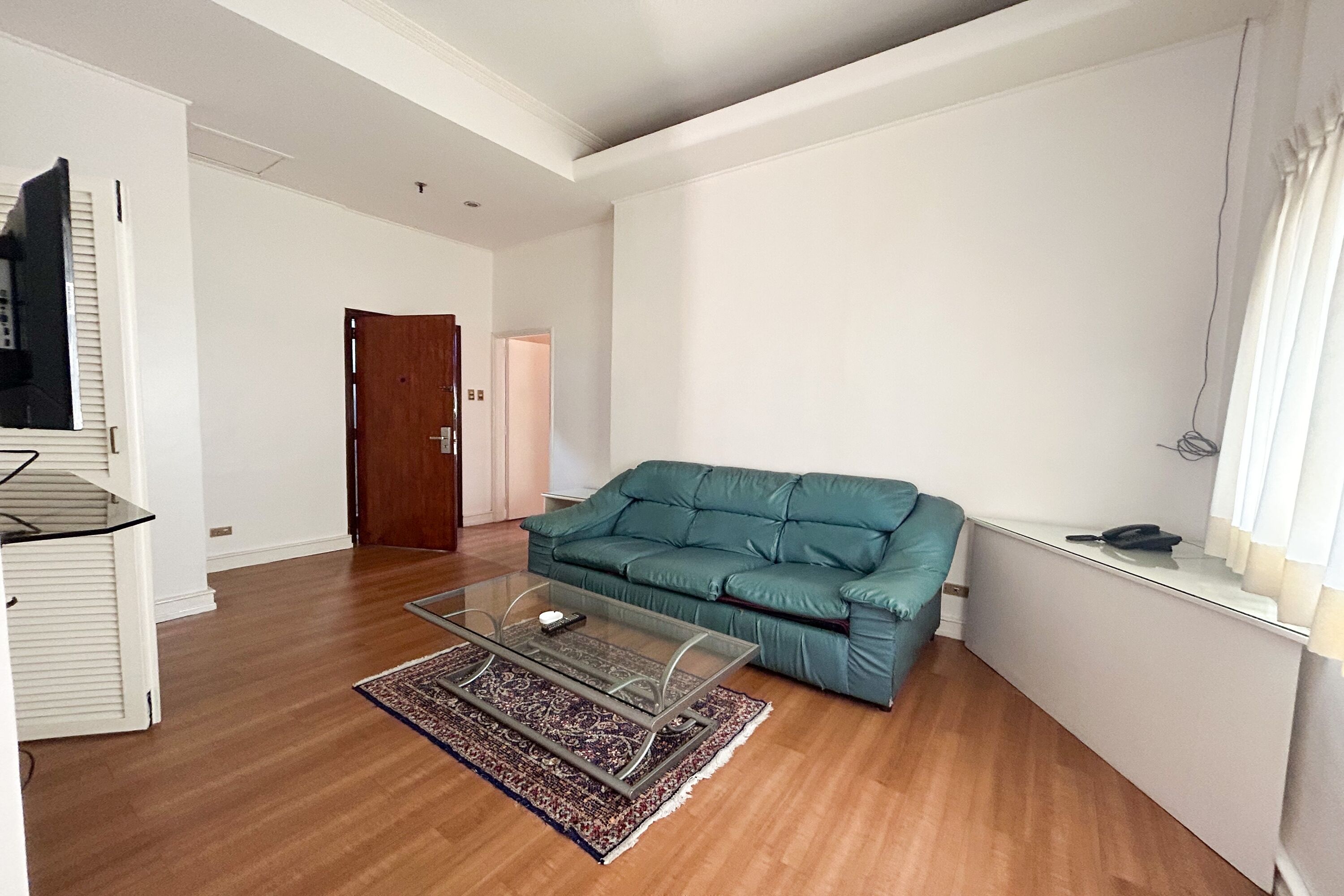 A living room with a teal sofa, a glass coffee table, and a wooden floor.