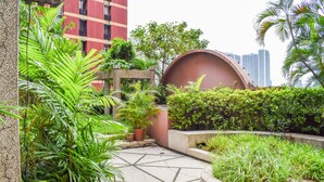 Un jardin sur le toit, agrémenté d’une végétation luxuriante, d’une fontaine circulaire et offrant une vue sur les gratte-ciel en arrière-plan.