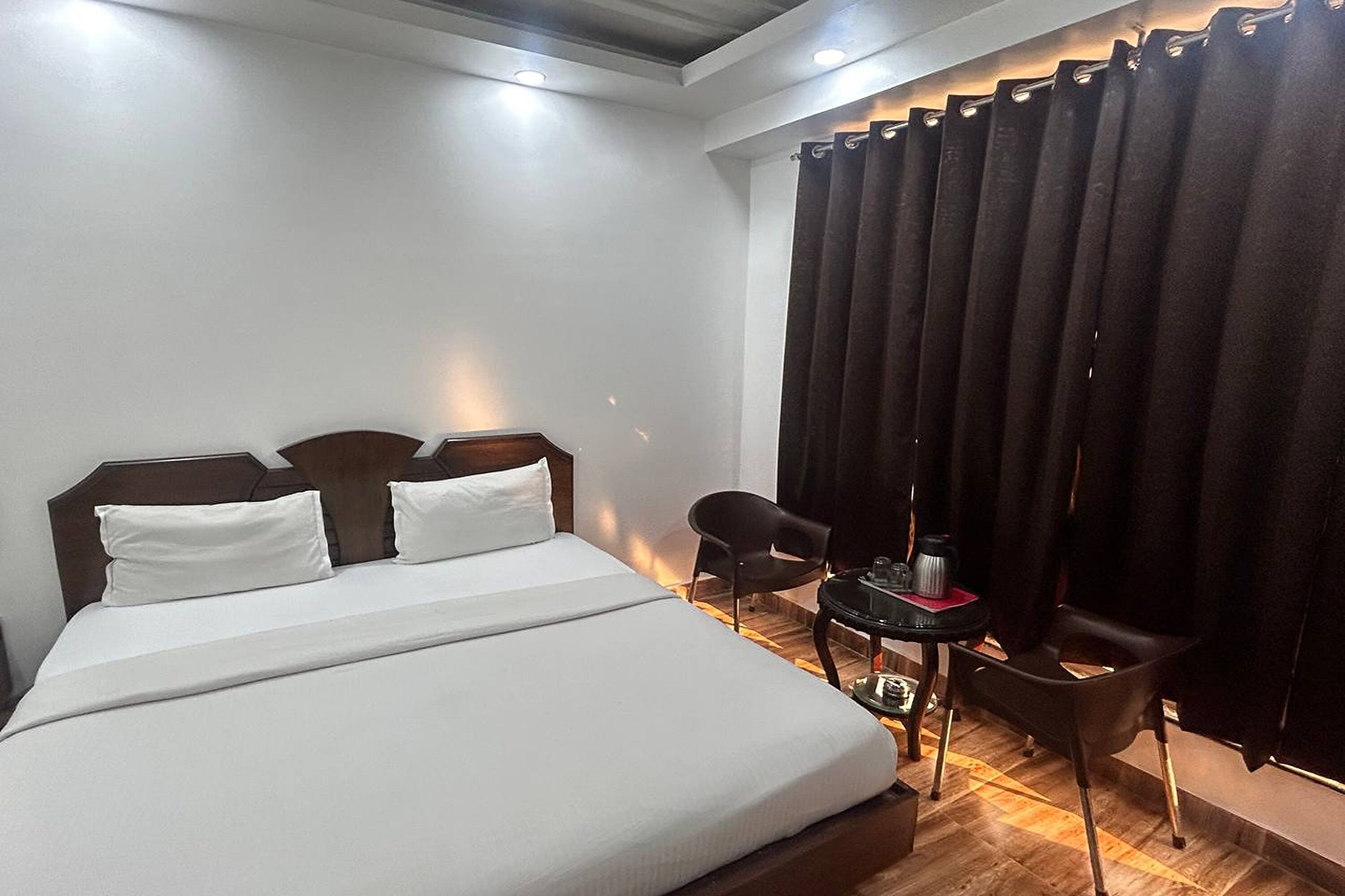 Ein Hotelzimmer mit einem großen Bett, einem kleinen Tisch mit Kaffeemaschine, zwei Stühlen und einem Vorhang.