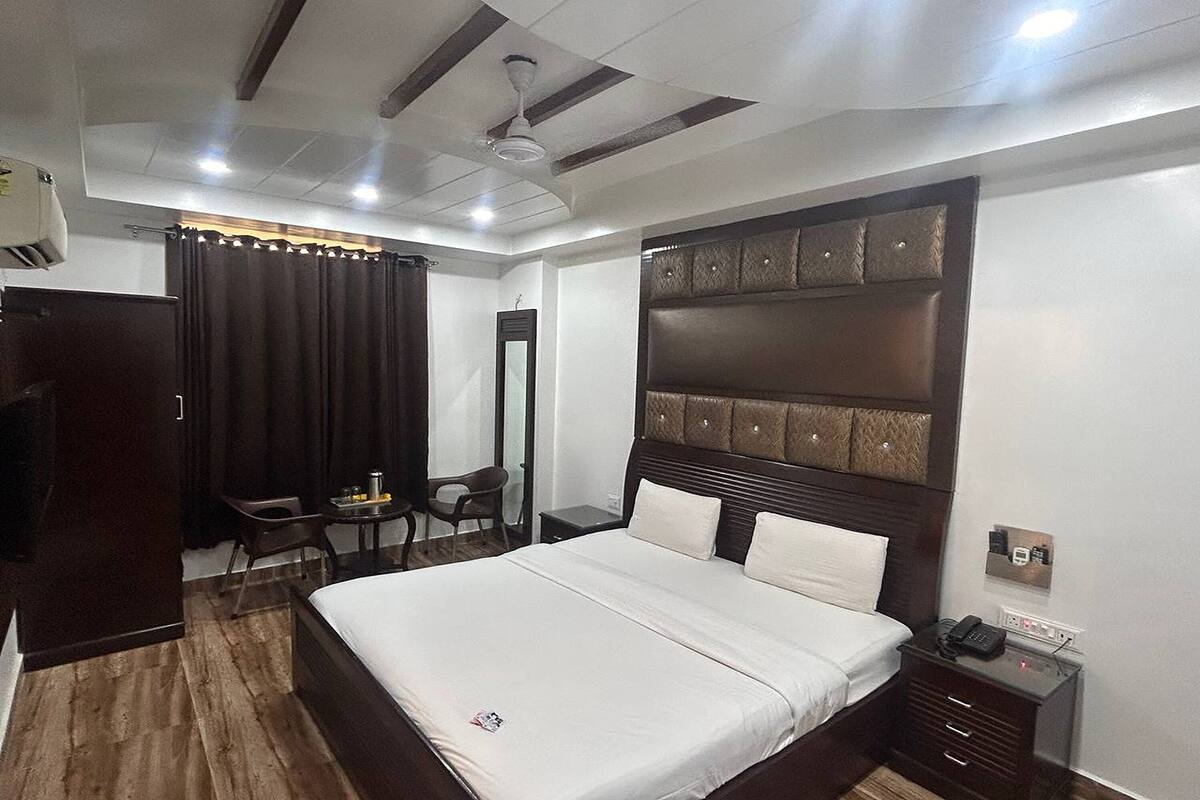 A hotel room with a large bed, a bedside table with a phone, a desk with a chair, a wardrobe, and a ceiling fan.