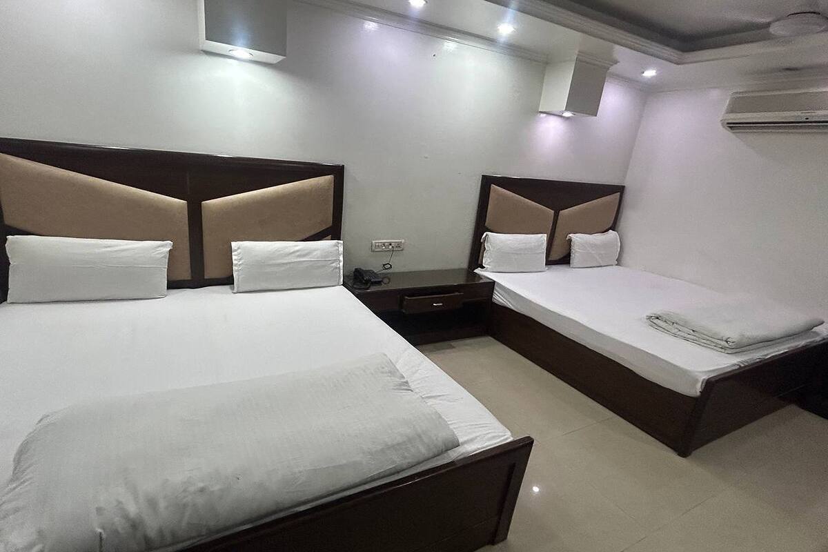A hotel room with two beds, a flat-screen TV, an air conditioning unit, and a bedside table with a lamp.