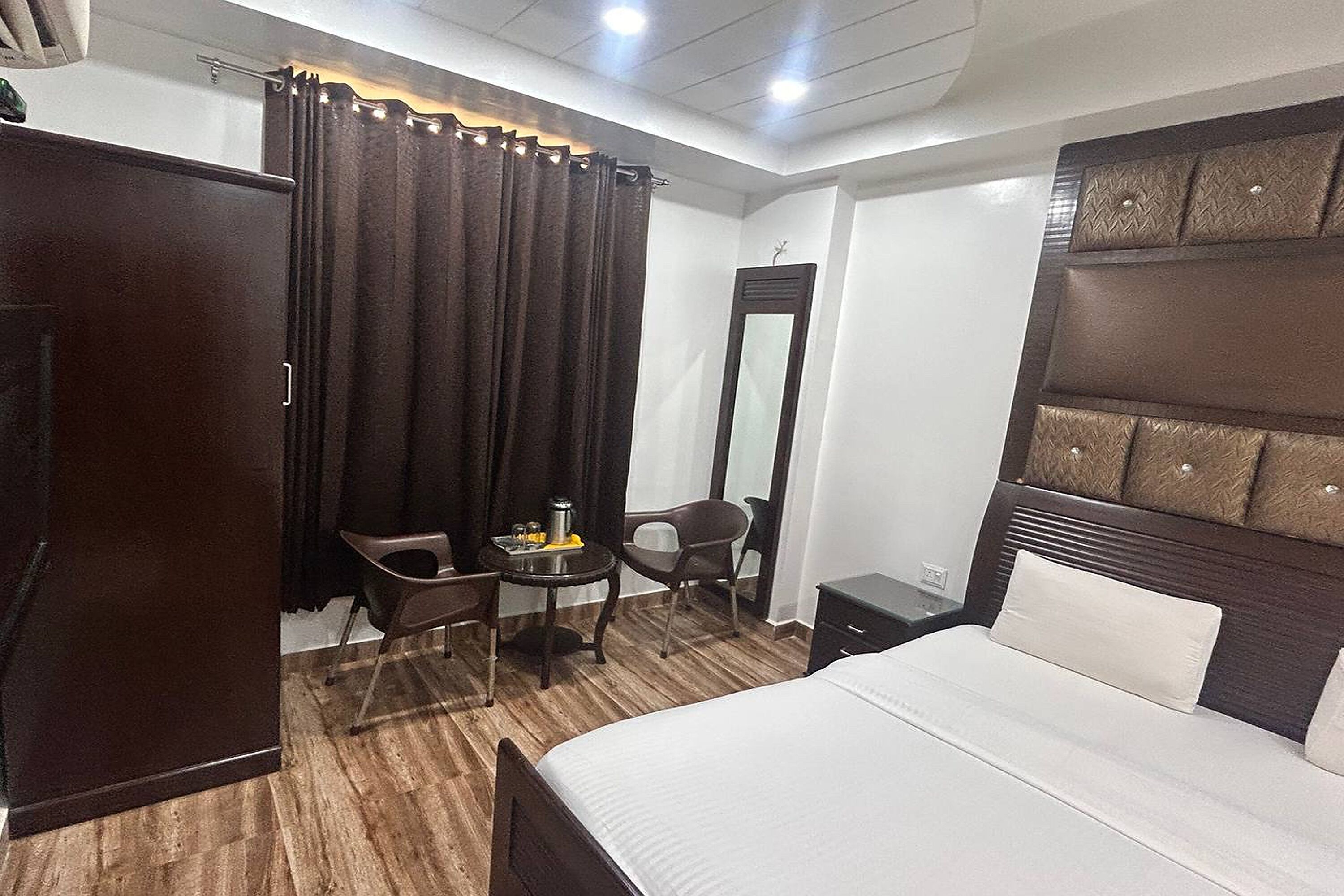 A hotel room with a bed, a desk, two chairs, a mirror, and a wardrobe.
