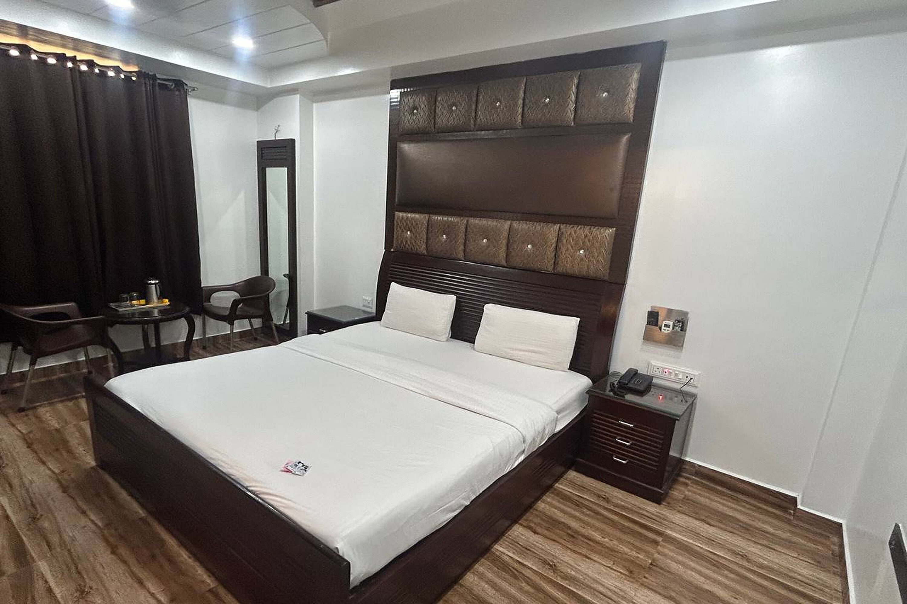 Ein modernes Hotelzimmer mit einem großen Bett, einem hölzernen Kopfteil, einem Nachttisch mit Telefon und einem Schreibtisch mit Stuhl.