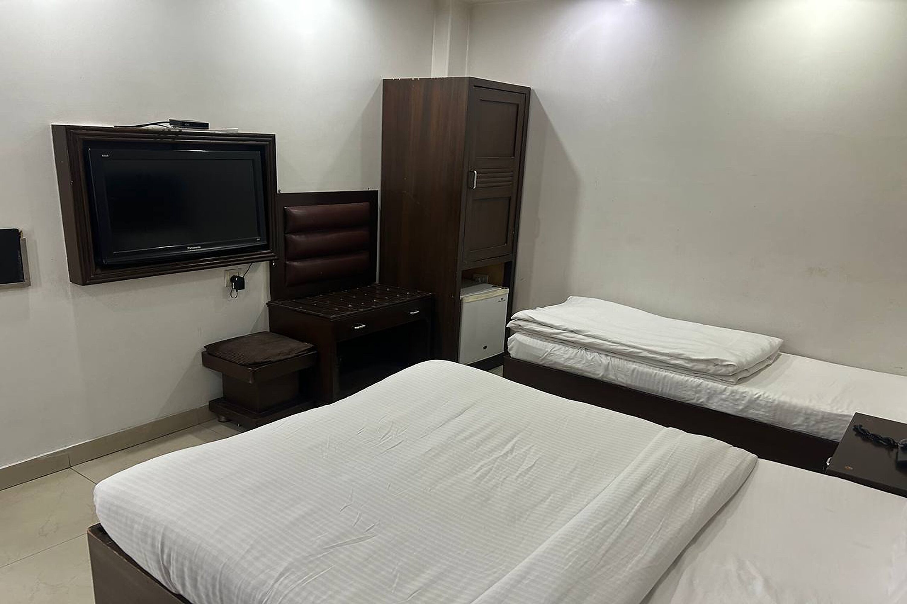 Habitación de hotel con dos camas, un escritorio con silla, un armario y televisión montada en la pared.