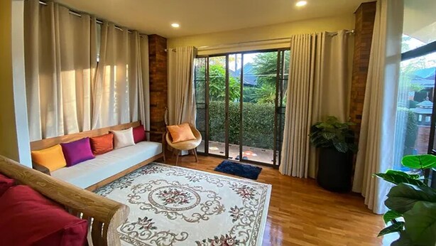 A spacious room with a large bed, a wooden bench, and a view of greenery through the glass doors. - Baan Wang Tarn (Hang Dong)