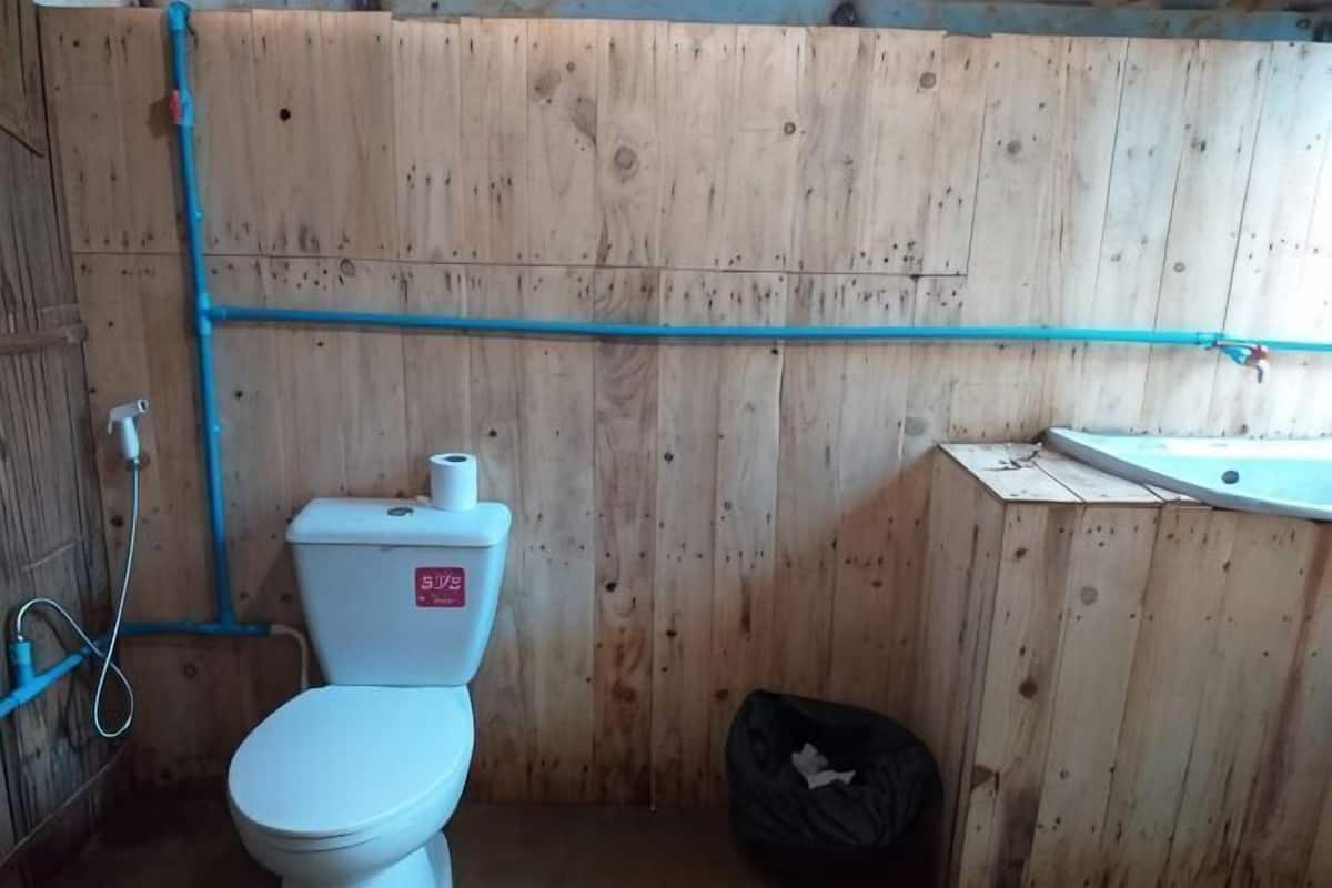 Un baño de madera con inodoro, lavamanos y un cubo de basura negro.