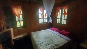 Una habitación con cama, ventana con cortinas y un banco de madera.