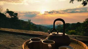 A wooden tray with a teapot and two cups on a wooden surface with a scenic view in the background.