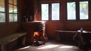 Una habitación rústica con chimenea de piedra, bancos de madera y ventanas amplias que dejan entrar luz natural.