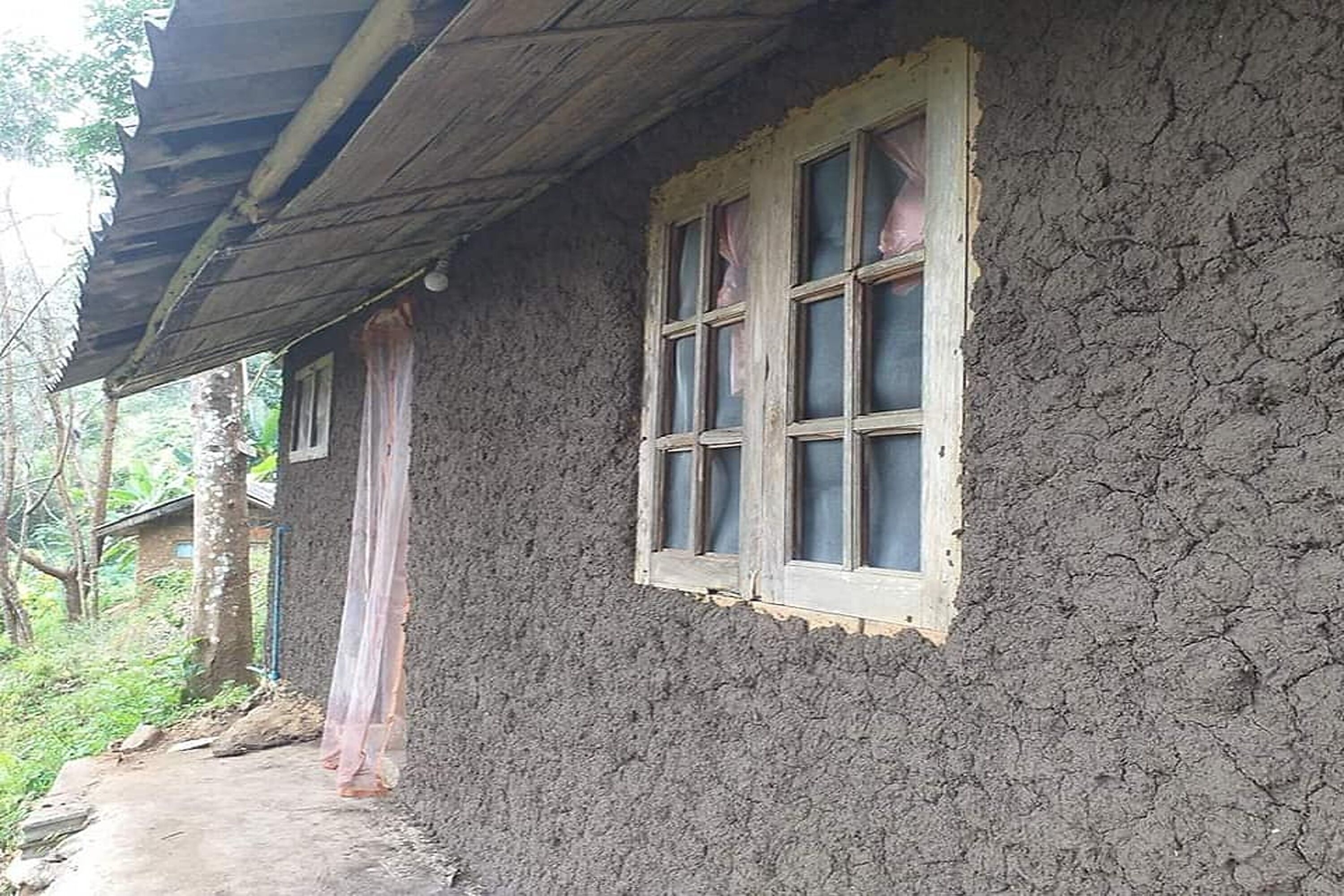 A rustic house with a thatched roof and a window with curtains.