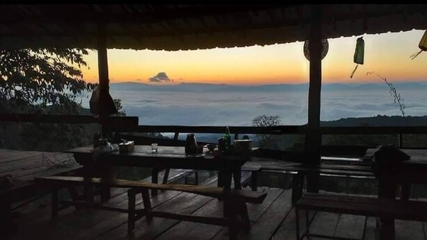Un área de estar al aire libre con mesas y bancos de madera, con vistas a un paisaje panorámico de un atardecer sobre el agua.