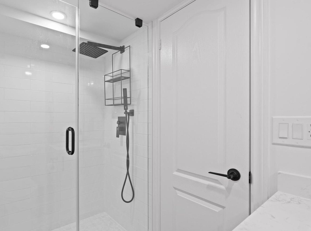 A modern bathroom with a glass shower enclosure, a white tiled wall, and a door with a handle.