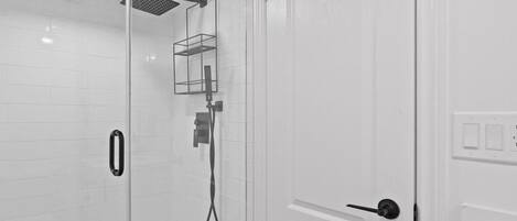 A modern bathroom with a glass shower enclosure, a white tiled wall, and a door with a handle.