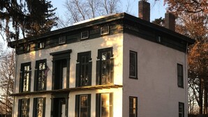 A two-story white building with black shutters and a brick chimney. - Historic McDonald Airbnb (Attica)