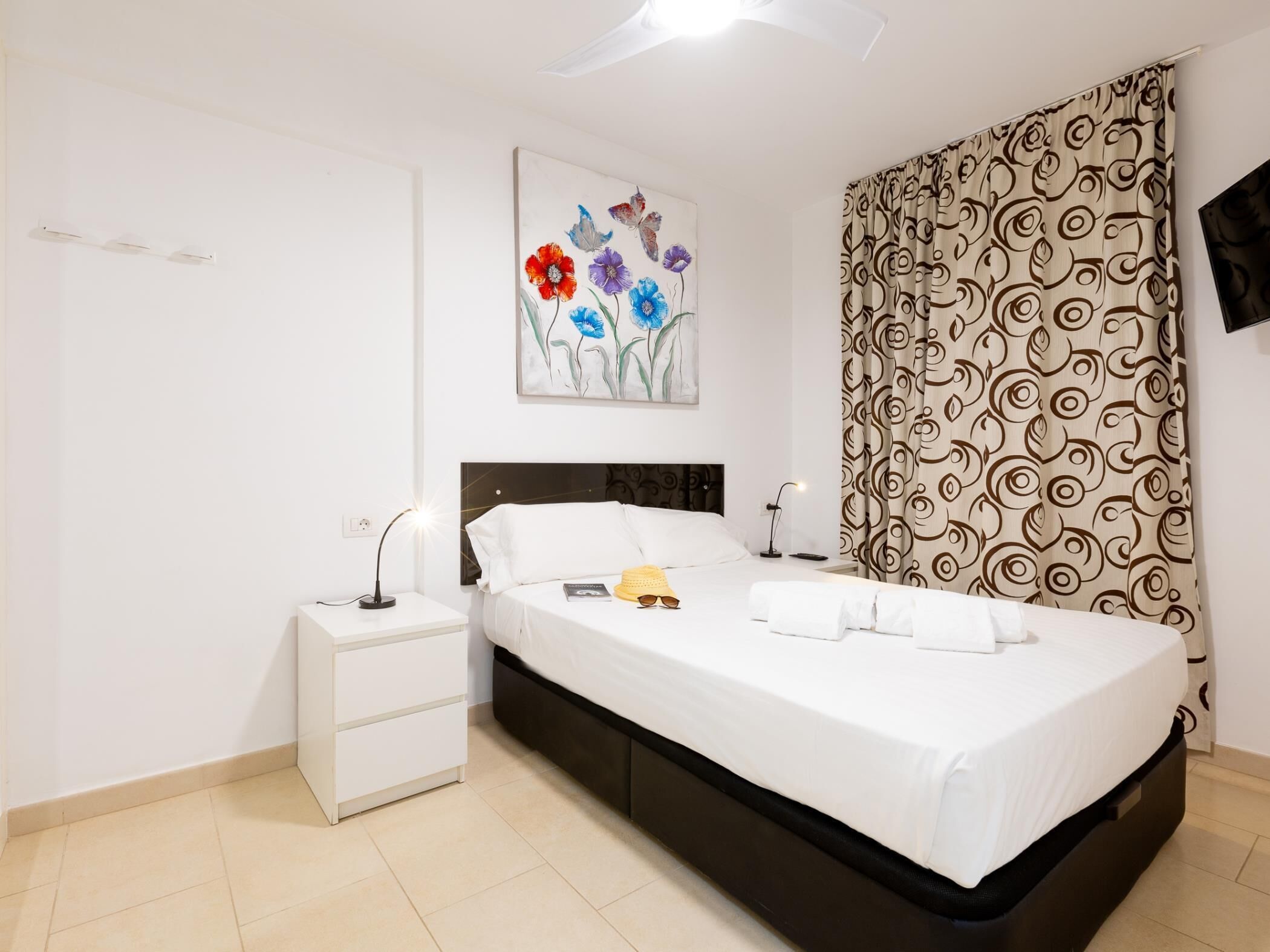 A bedroom with a bed, nightstands, a wall-mounted painting, and patterned curtains.