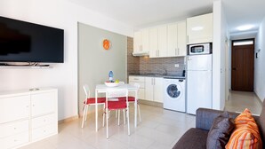 A compact living space with a dining area, kitchenette, and a sofa with cushions.