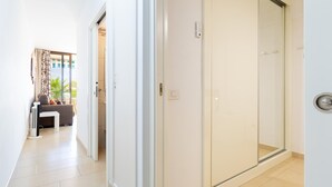 A hallway with a sliding glass door leading to a bathroom, a sofa in a sunlit room, and a white wall with a thermostat.