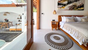 Un dormitorio moderno con una cama grande, cabecera de madera, alfombra redonda tejida y un cuadro en la pared.