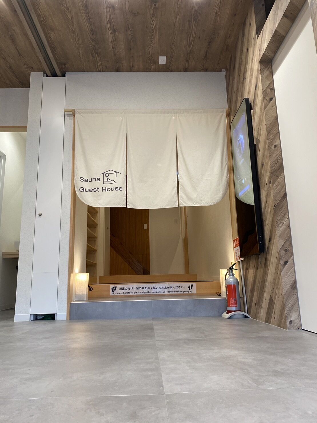 A guest entrance with a sauna sign, a fire extinguisher, and a wooden floor.