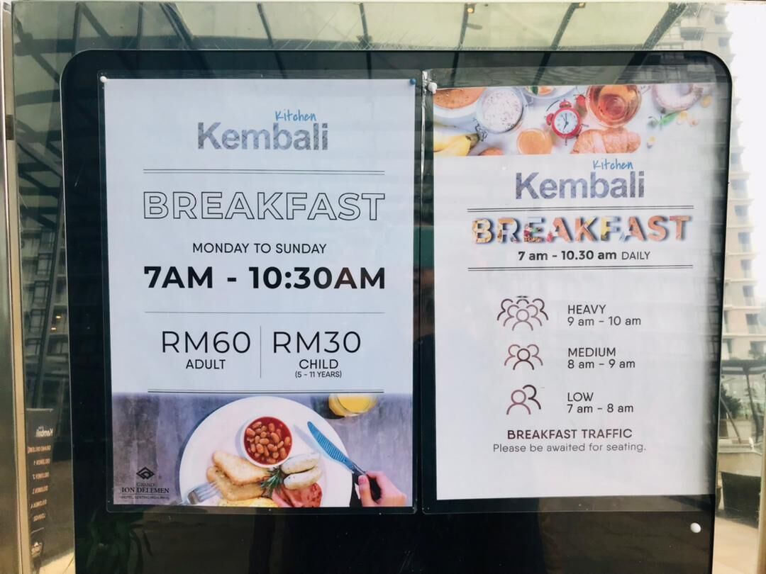 A breakfast menu board for Kembali, listing times and prices for adults and children.