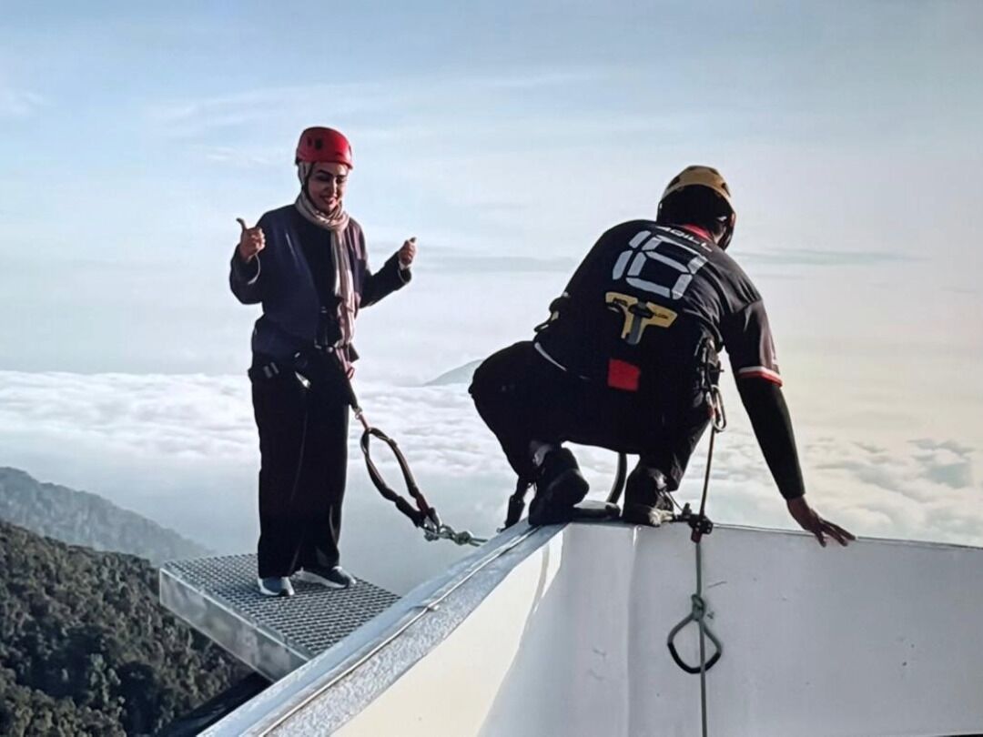 Two individuals on a high platform with a rope, overlooking a mountainous landscape.