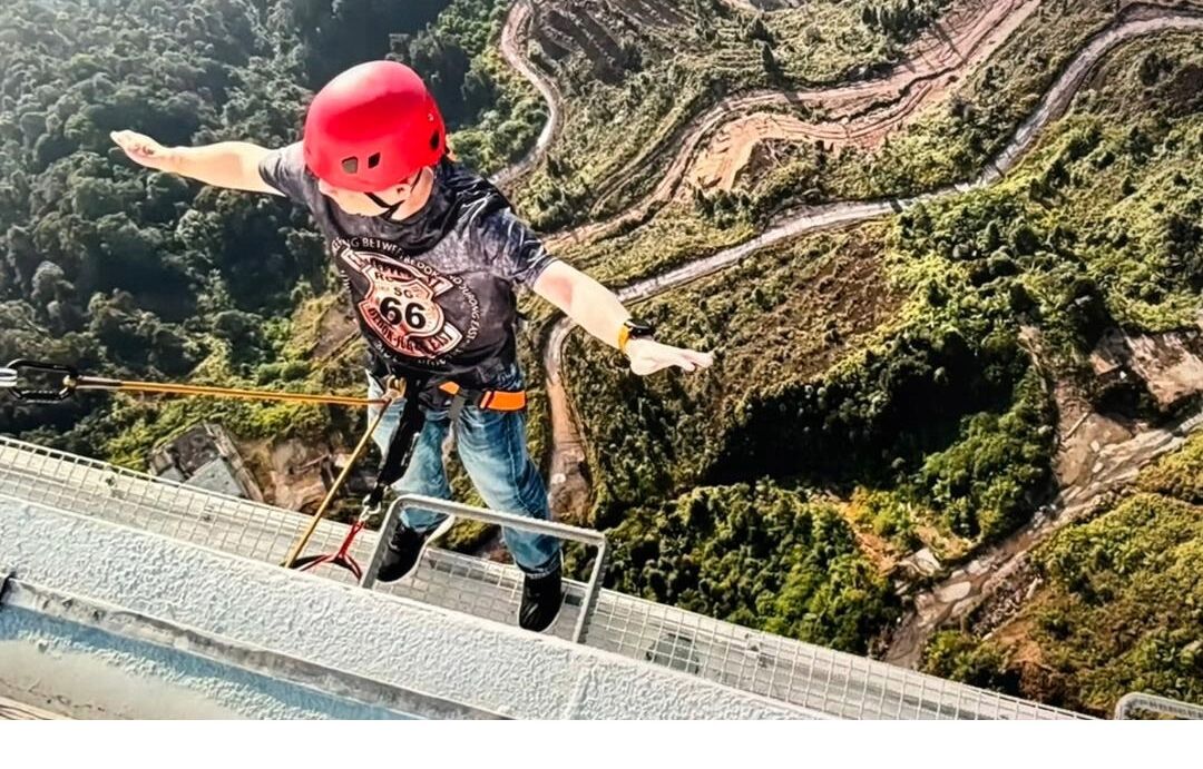 A person bungee jumping with a helmet and harness, with a mountainous landscape in the background.