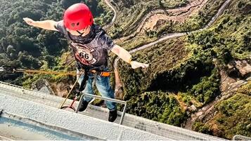 A person bungee jumping with a helmet and harness, with a mountainous landscape in the background.