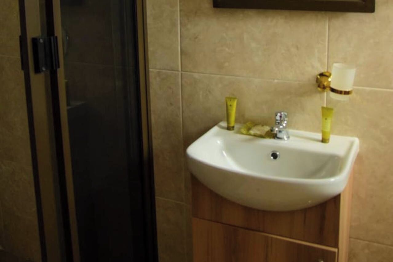 Un baño con lavamanos blanco, mueble de madera y cabina de ducha de cristal.