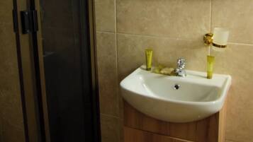 Un baño con lavamanos blanco, mueble de madera y cabina de ducha de cristal.