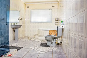 Bathroom features a large sink, toilet, and window with blinds, set against a backdrop of decorative tiles and a geometric tile floor.