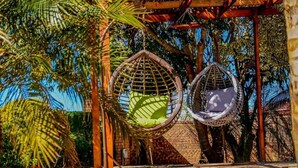 Dos sillones colgantes de mimbre con cojines bajo una pérgola de madera.
