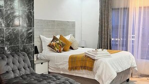 Un dormitorio moderno con cama, un sillón capitonado y una mesita de noche.