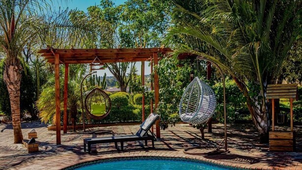 Zona de piscina con una pérgola de madera, una hamaca colgante y una silla de descanso.