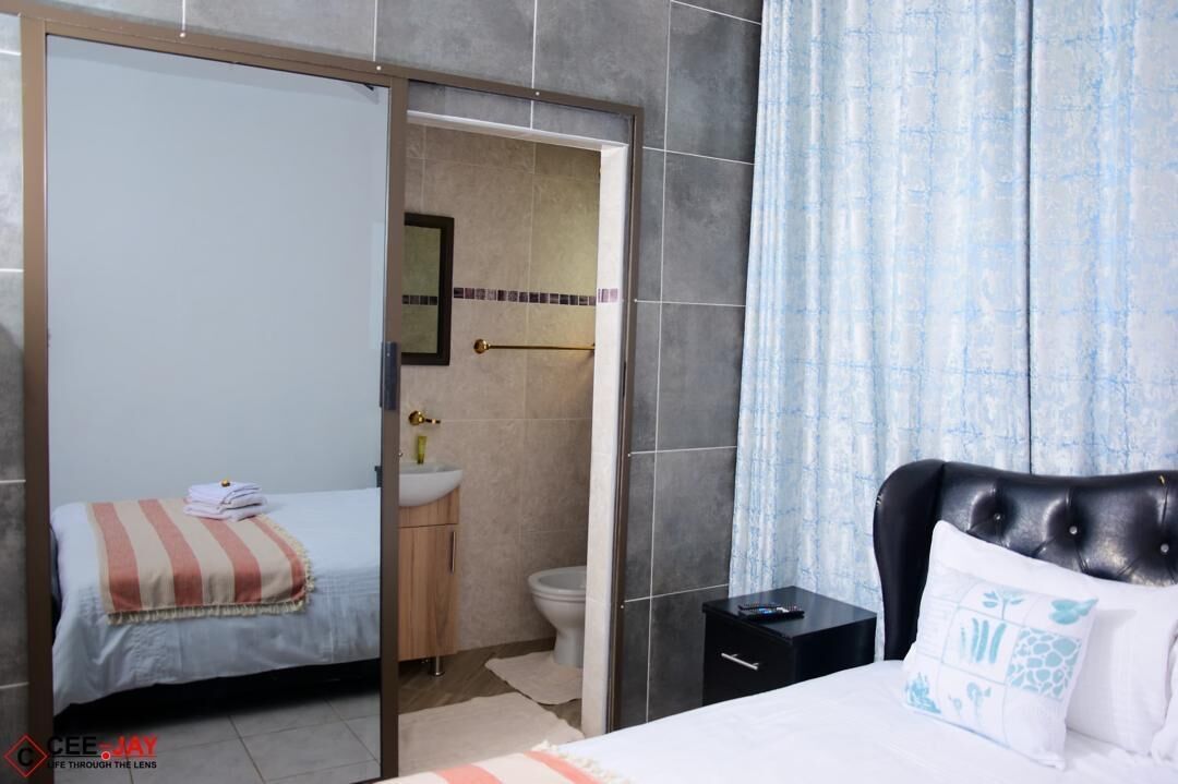 A bedroom with a bed, a nightstand, a bathroom with a sink and toilet, and a sliding door to another room.