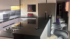 Una cocina moderna con una isla central, electrodomésticos de acero inoxidable y taburetes negros.