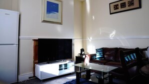 Un salon avec un téléviseur à écran plat, une table basse en verre, un canapé et un tableau encadré accroché au mur.