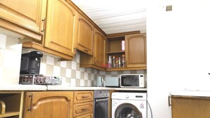 Une cuisine compacte dotée de meubles en bois, d’une machine à café, d’un four à micro-ondes et d’un lave-linge.