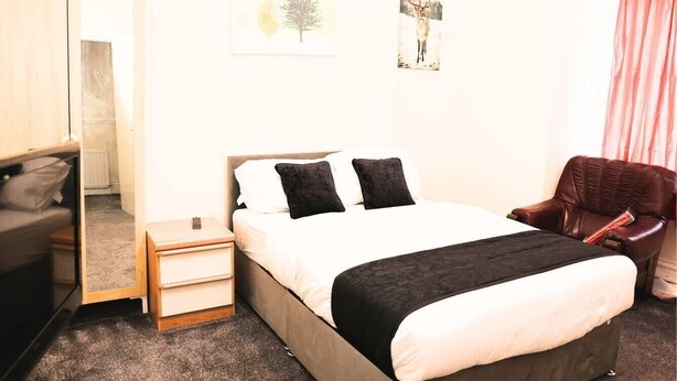 Une chambre à coucher comprenant un lit, des tables de chevet, une chaise, un miroir et un tableau accroché au mur.