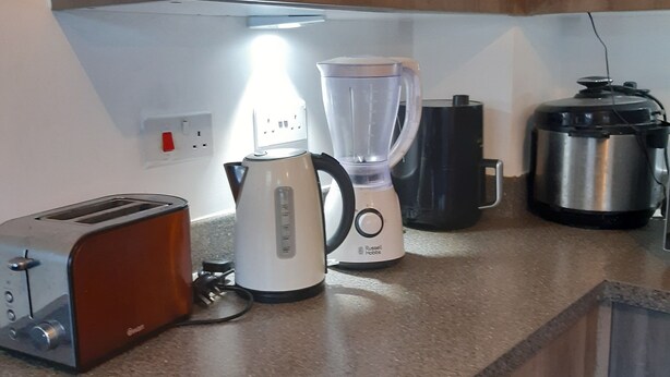 Een keuken met houten kastjes, een broodrooster, een waterkoker, een blender en een snelkookpan op het aanrecht.