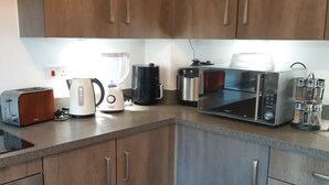 Een moderne keuken met houten kastjes, een magnetron, broodrooster, waterkoker en koffiezetapparaat.