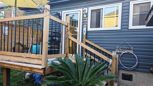 A wooden deck with a yellow umbrella, a sign reading "Whale Cove", and a house with two windows and a door.