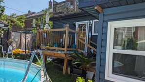 A backyard with a swimming pool, a wooden deck, and a house with a window.