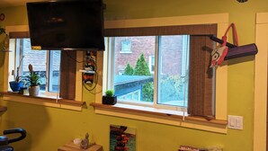 A room with a television mounted above a window, potted plants on the windowsill, a small statue on a shelf, and a poster on the wall.
