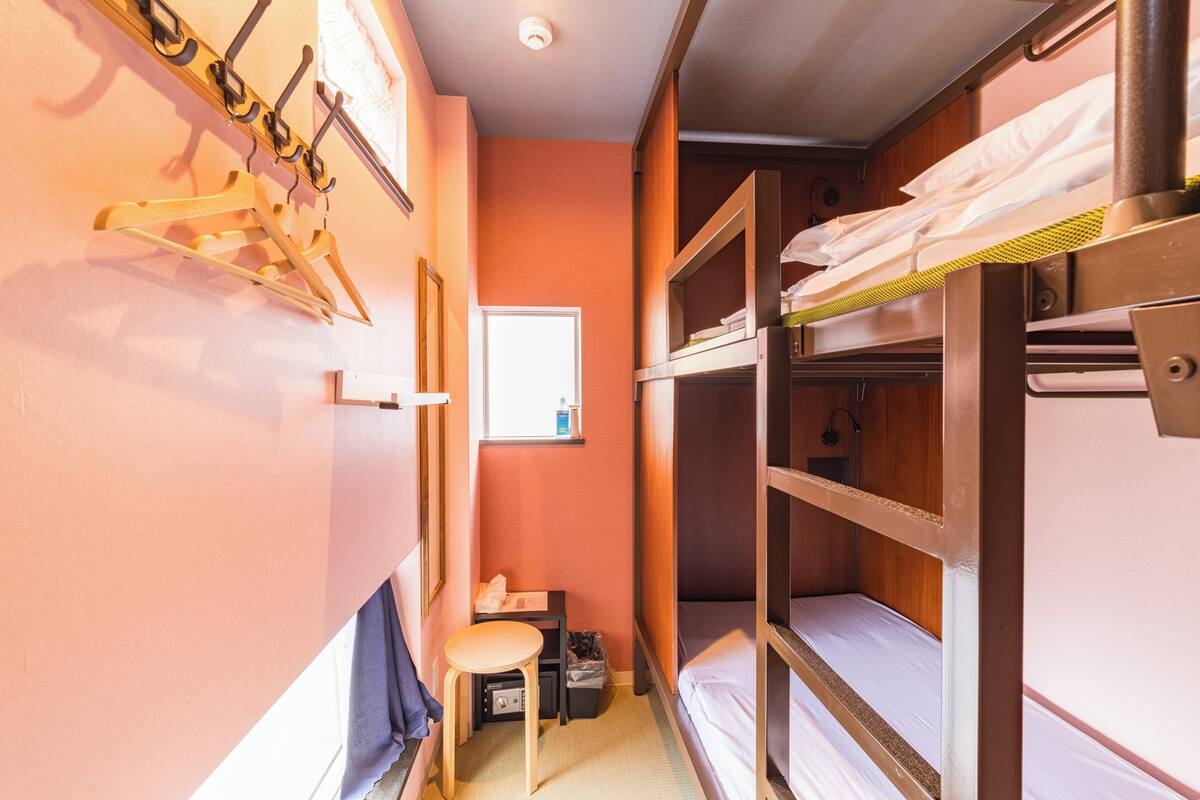 A narrow room with bunk beds, a small table, and a window.