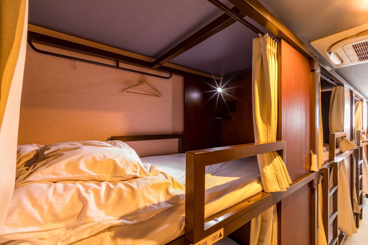 A bunk bed with a hanging garment rack and a window with curtains.