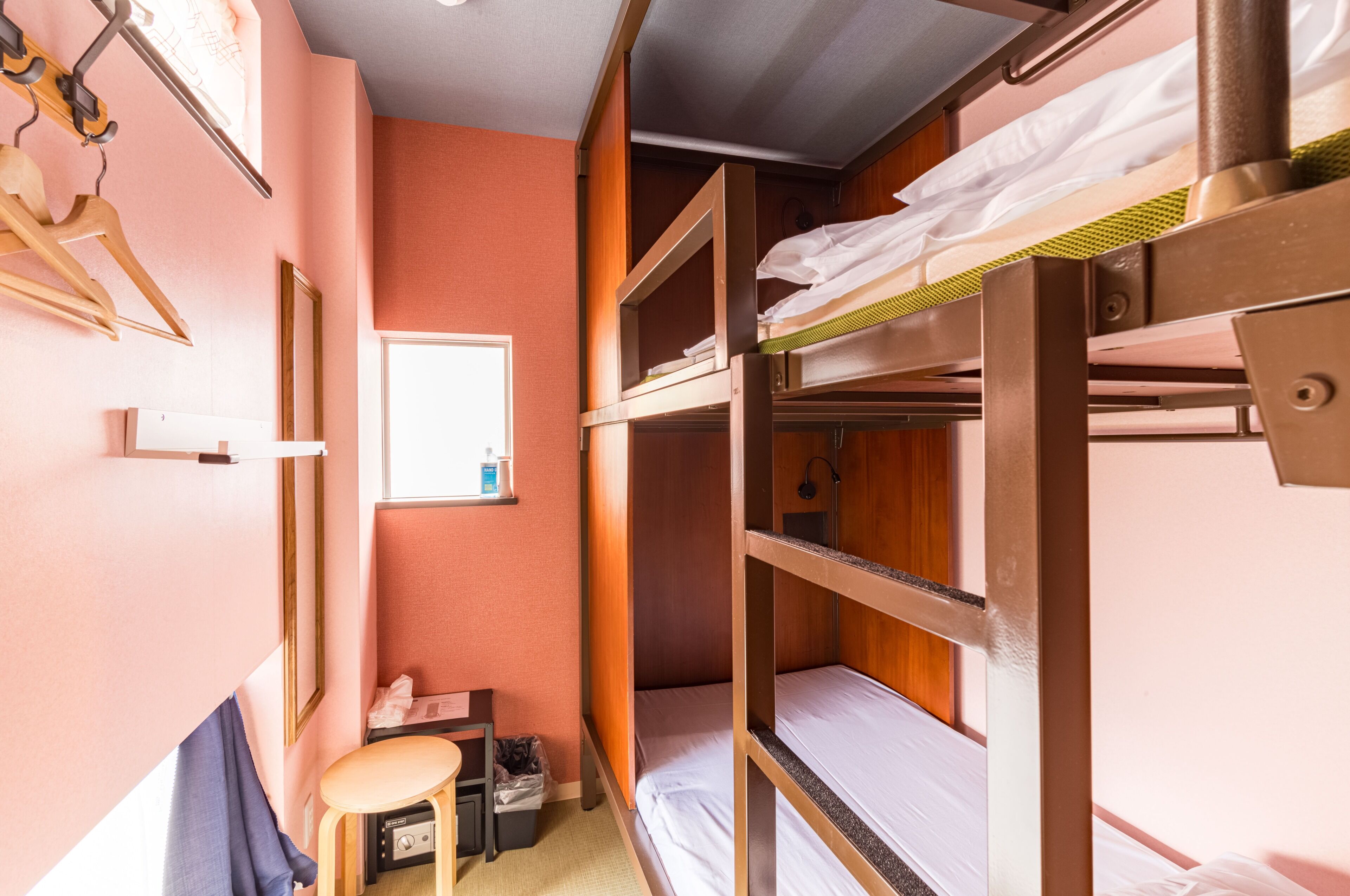 A bunk bed room with a desk and chair, a small window, and a hanging coat rack.